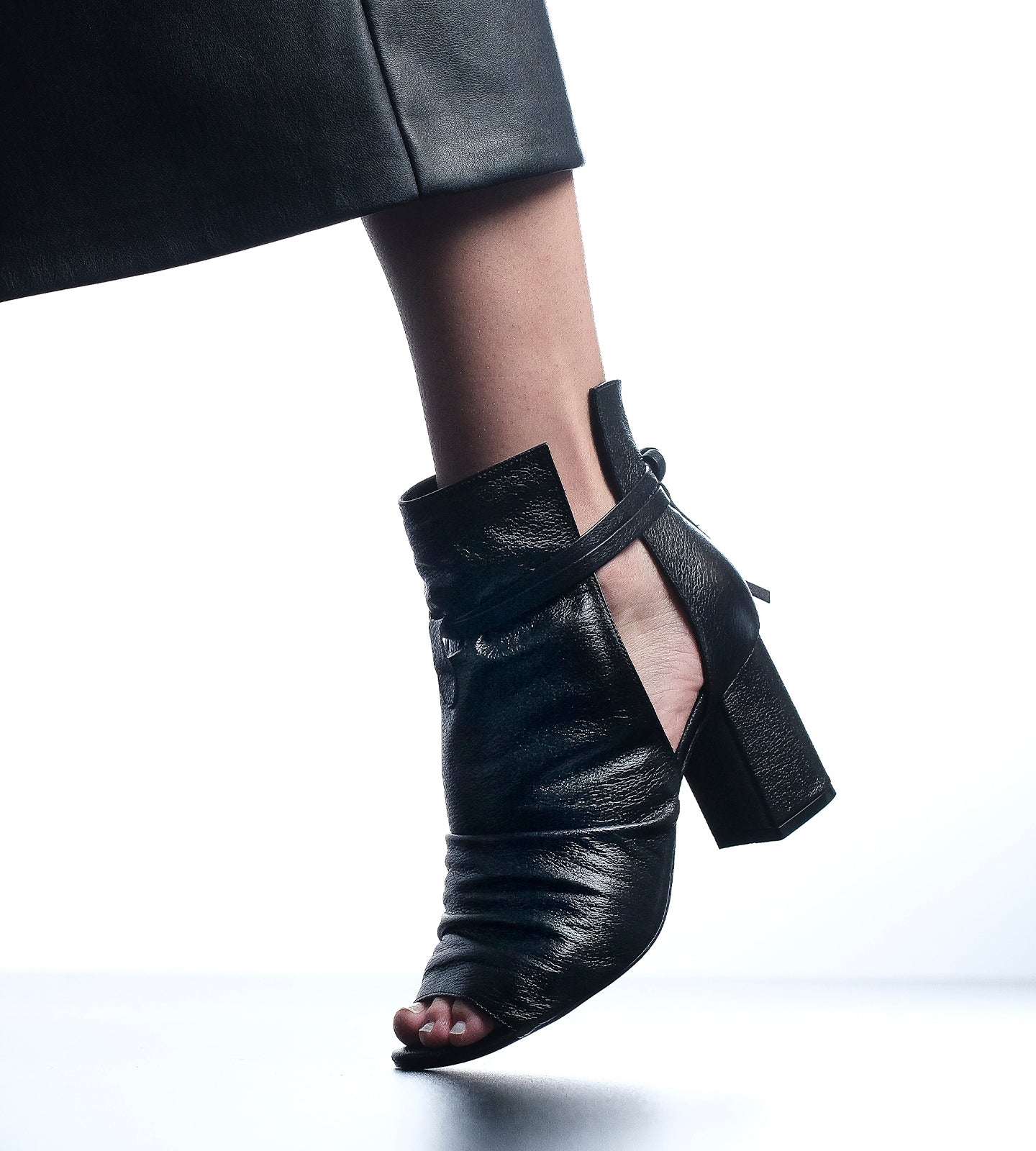 Ankle Boot Open Toe feminina em couro preto com salto bloco de 7 cm, cabedal drapeado, recortes laterais e amarração no tornozelo.