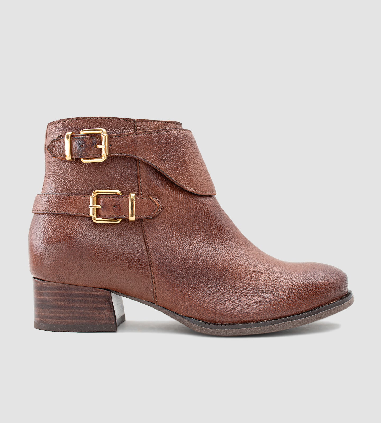 Bota feminina de cano curto em couro legítimo marrom, com acabamento texturizado e design elegante, destacando duas fivelas metálicas douradas que agregam sofisticação ao modelo. O salto grosso baixo, aliado ao solado emborrachado, proporciona conforto e segurança no uso diário. Versátil e atemporal, essa bota é ideal para compor looks clássicos com um toque moderno, perfeita para dias mais frios ou produções urbanas com personalidade.