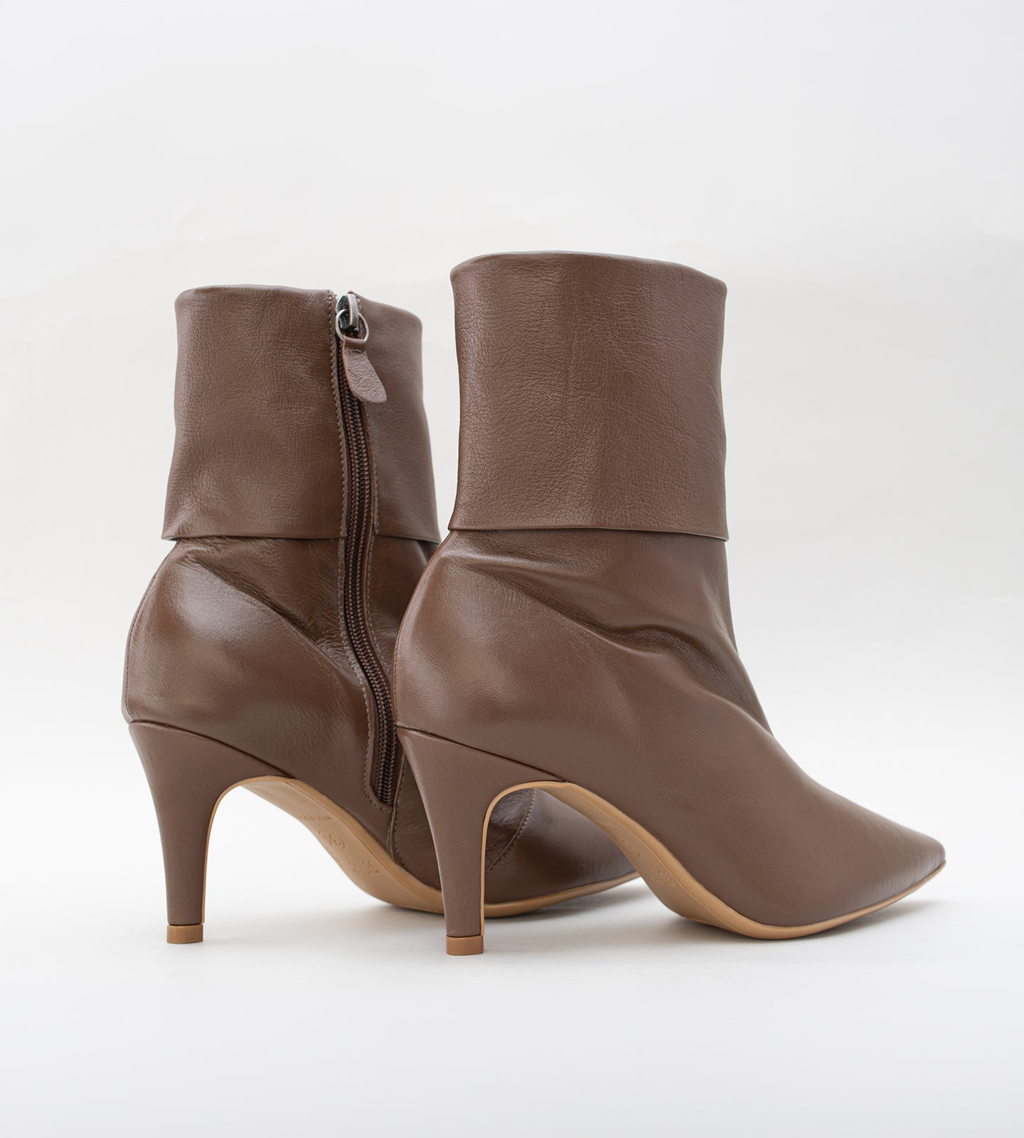 Bota feminina de cano médio em couro marrom. O modelo possui bico fino, salto fino de 8cm e um detalhe de dobra na parte superior do cano.