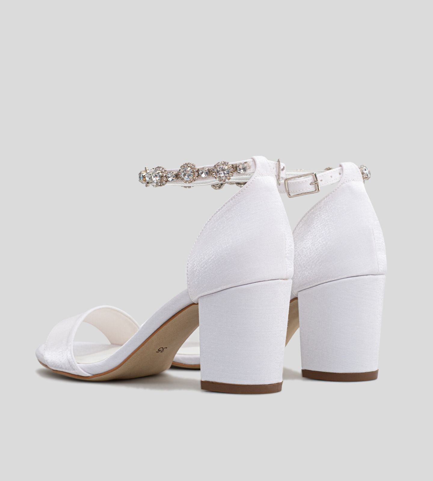 Sandália de noiva branca com salto bloco médio, tira frontal larga e tornozeleira adornada com pedrarias brilhantes, ideal para casamentos e ocasiões especiais.