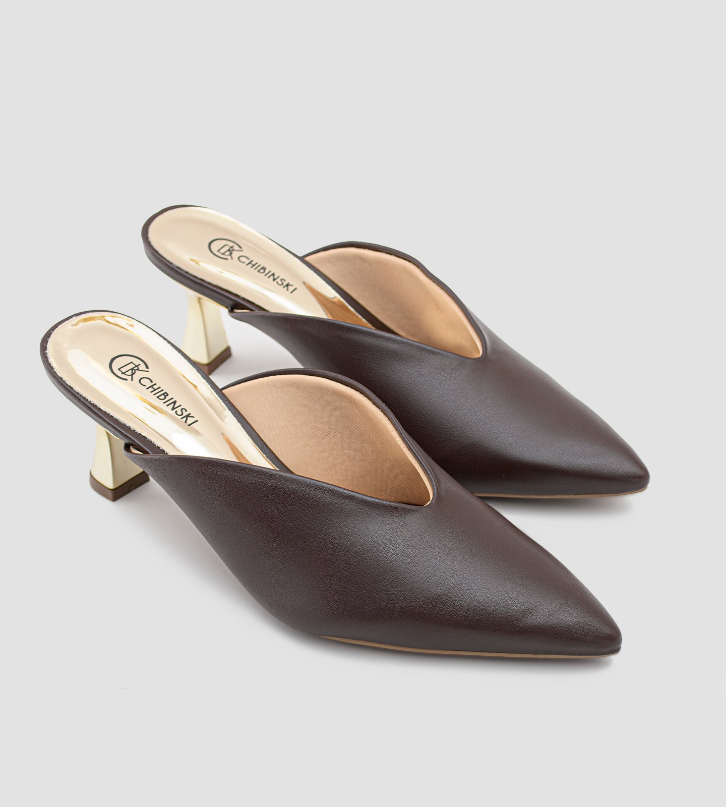 Mule marrom em napa com bico fino e salto dourado escultural de 7cm, combinando design moderno, elegância e conforto.