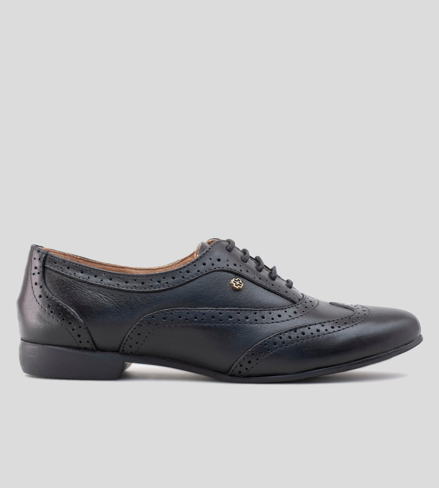 Sapato Oxford feminino em couro preto, com design clássico e detalhes brogue perfurados. Modelo elegante e versátil, possui fechamento por cadarço e solado baixo, ideal para compor looks sofisticados e casuais com conforto.