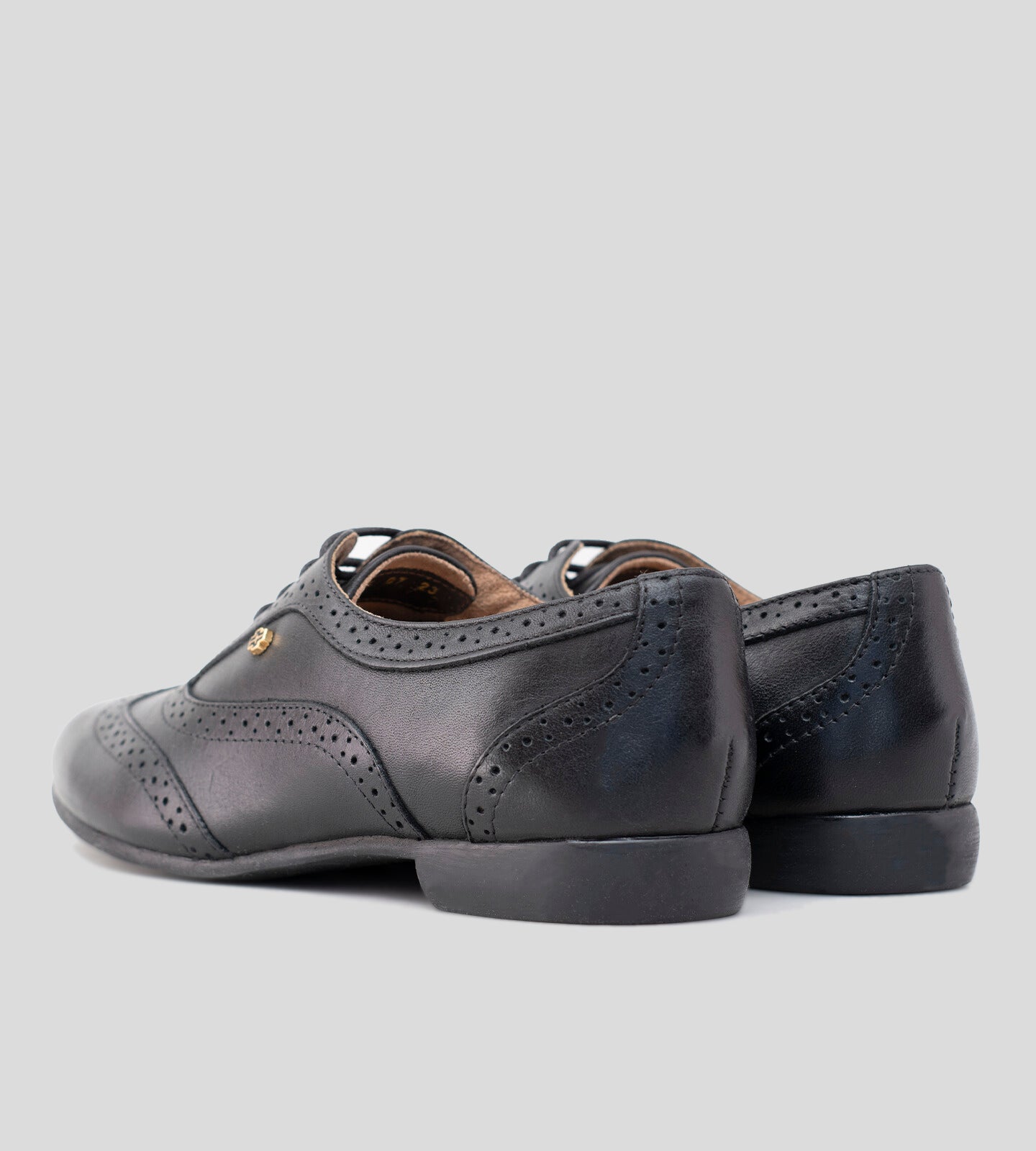 Sapato Oxford feminino em couro preto, com design clássico e detalhes brogue perfurados. Modelo elegante e versátil, possui fechamento por cadarço e solado baixo, ideal para compor looks sofisticados e casuais com conforto.