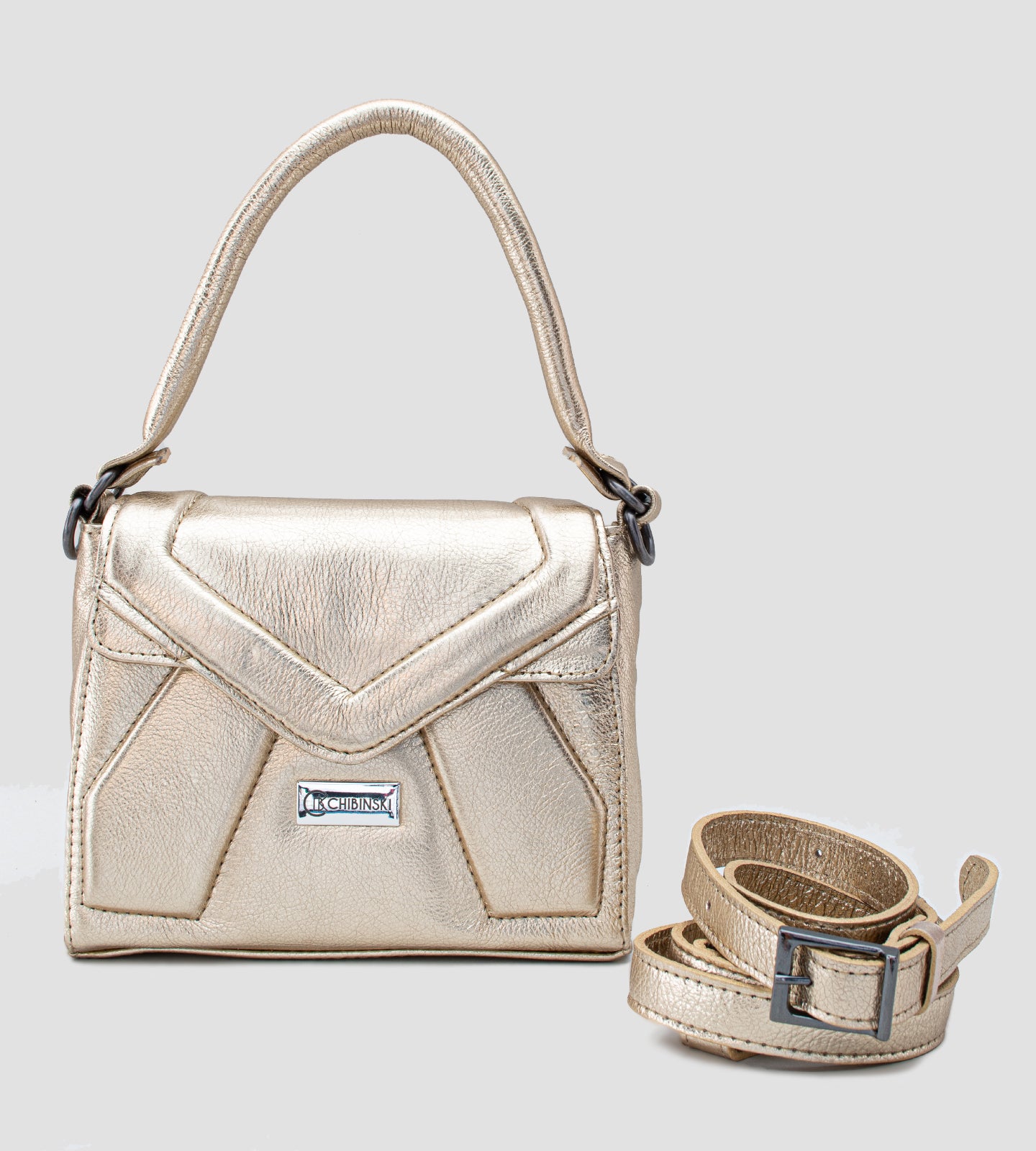 Imagem de uma bolsa feminina pequena da marca Chibinski, confeccionada em couro legítimo dourado. O design moderno apresenta linhas geométricas marcantes, acabamento metálico sofisticado e fecho frontal com a logo da marca em destaque. A bolsa possui alça de mão fixa, ideal para complementar looks elegantes em ocasiões especiais, como festas e casamentos.