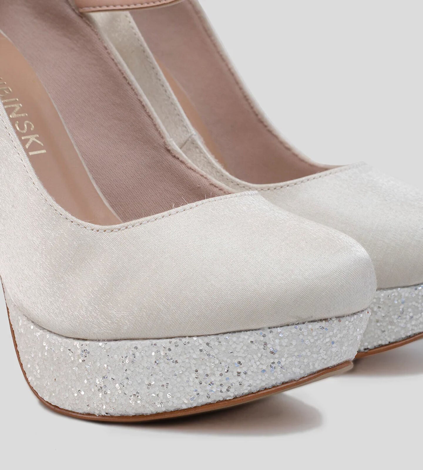 Sapato tipo boneca com bico redondo, salto fino de 12 cm e meia pata de 3 cm. Apresenta aplicações de glitter branco Luma, feito em tecido cetim na cor off white. Inclui ajuste com tornozeleira no dorso do pé.