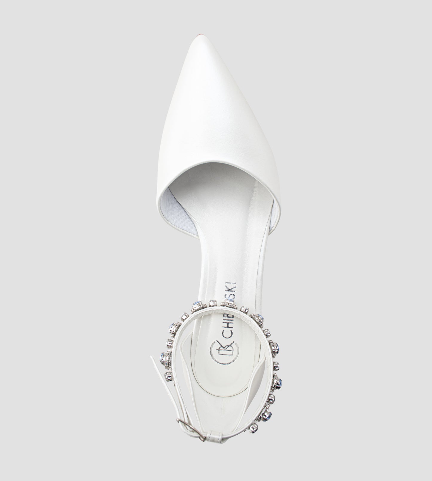 Sapato de noiva em couro branco perolado com bico fino, salto bloco médio e pulseira no tornozelo adornada com cristais azul-claro, ideal para casamento, fotografado em fundo cinza claro.
