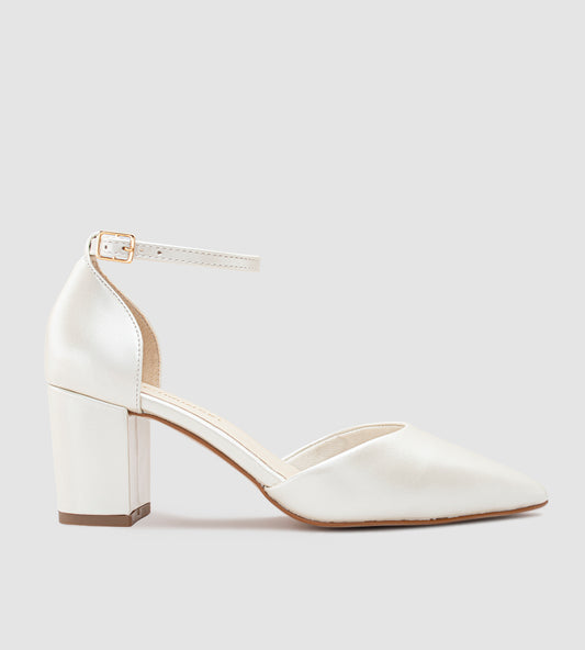 Imagem de um scarpin de noiva na cor off-white com acabamento em couro perolado. O sapato possui bico fino, salto bloco médio e uma tira com fivela dourada ajustável no tornozelo. O design é elegante e minimalista, ideal para casamentos e eventos especiais.