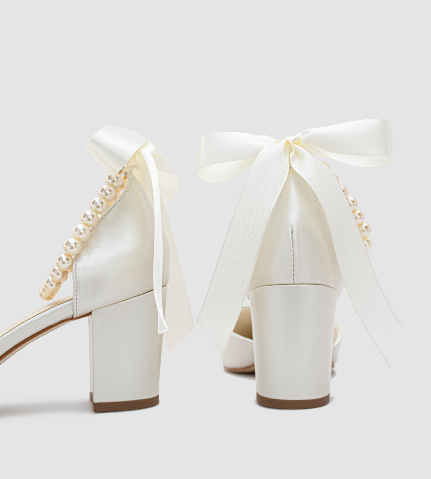 Sandália de noiva em couro perolado off white com salto bloco de 7cm, bico fino e tornozeleira de pérolas com laço de cetim, ideal para casamento.