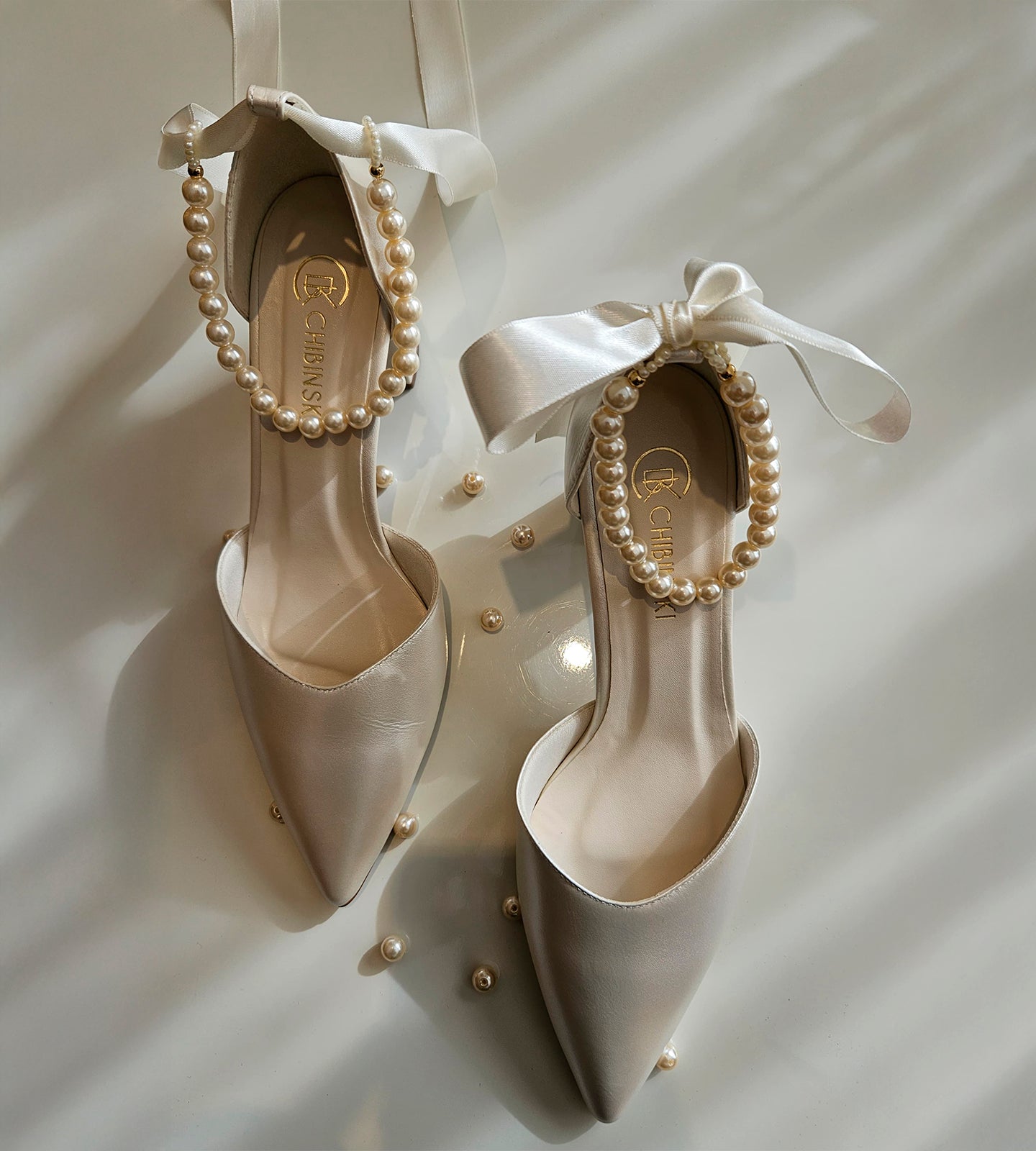 Sandália de noiva em couro perolado off white com salto bloco de 7cm, bico fino e tornozeleira de pérolas com laço de cetim, ideal para casamento.
