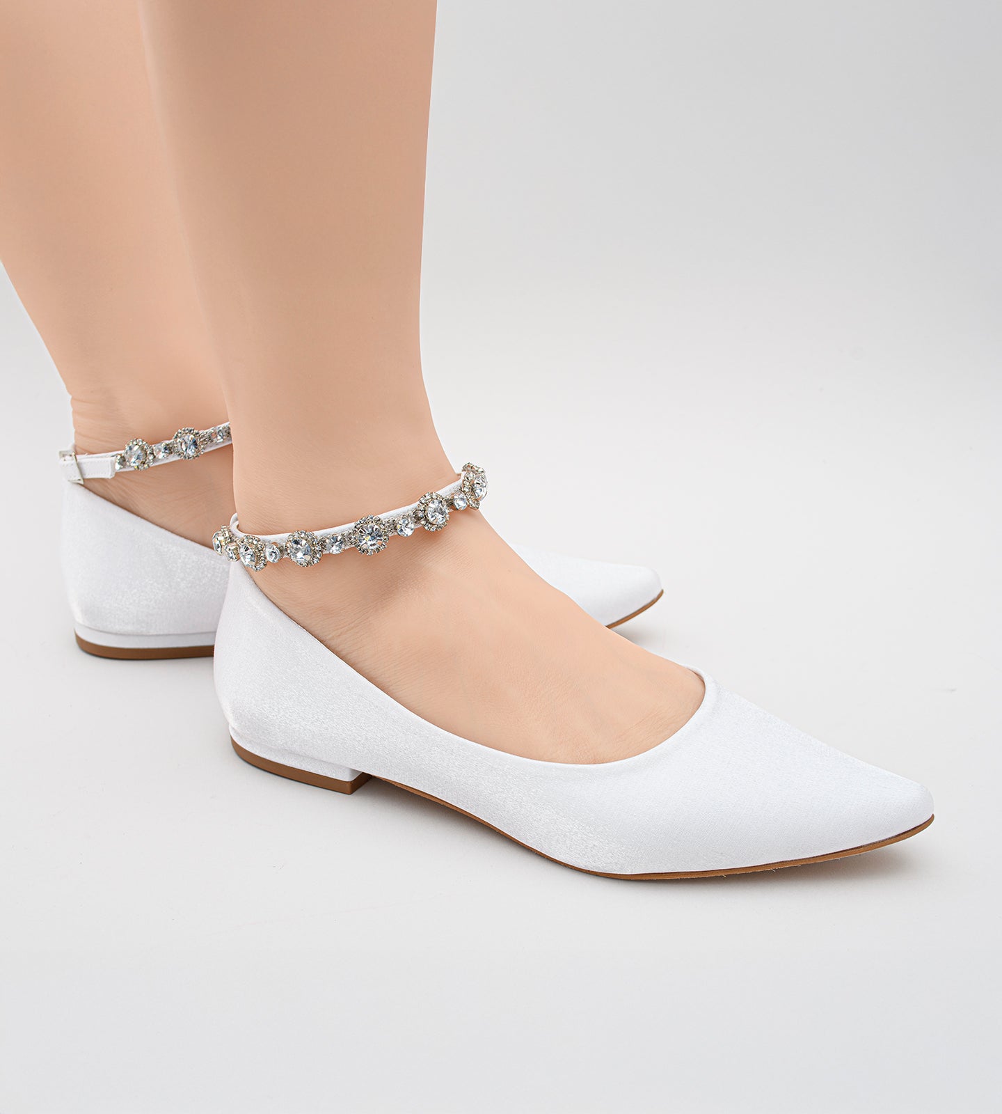 Sapatilha de noiva em material acetinado com acabamento perolado, design minimalista e tornozeleira delicada de strass, ideal para casamentos ao ar livre como no campo ou na praia.