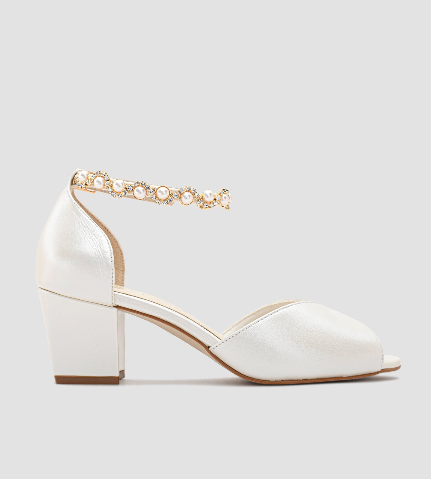 Sandália de noiva em couro perolado off-white com salto grosso de 5 cm, alça no tornozelo com fivela ajustável e tornozeleira de strass, combinando conforto, elegância e brilho sutil — ideal para cerimônias e festas de casamento.
