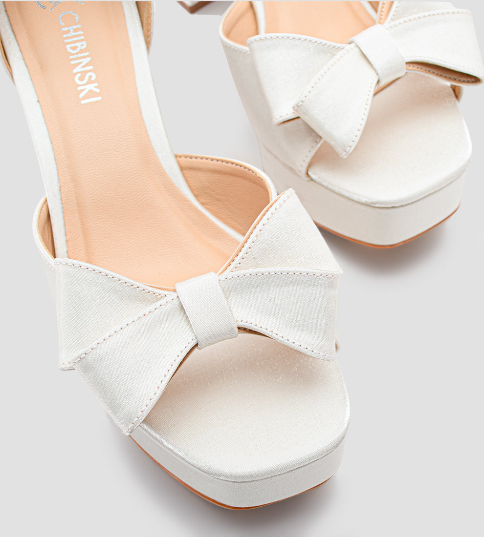 Sandália plataforma em velvet branco com brilho suave, laço frontal, salto bloco de 8 cm e fivela ajustável no tornozelo, ideal para noivas e ocasiões especiais.