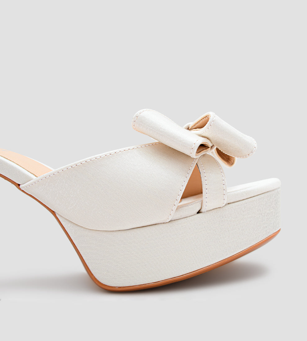 Sandália plataforma em velvet branco com brilho suave, laço frontal, salto bloco de 8 cm e fivela ajustável no tornozelo, ideal para noivas e ocasiões especiais.