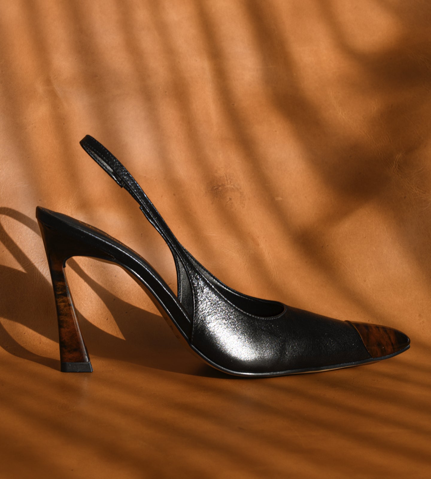 Scarpin slingback feminino de couro preto com salto alto fino de 10 cm, bico fino com ponteira marrom e tira no calcanhar, modelo elegante para trabalho, eventos e ocasiões formais.
