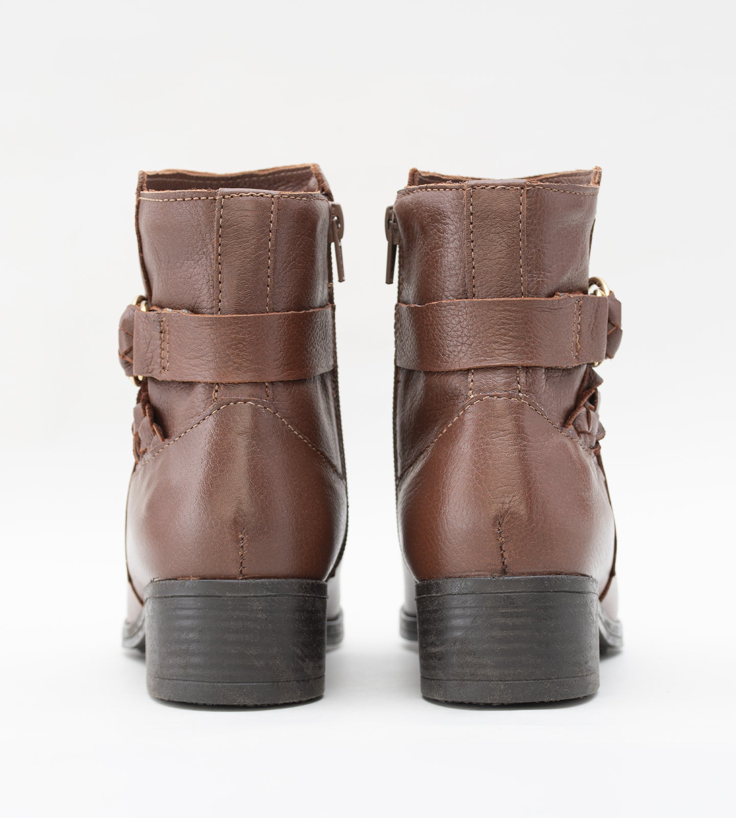 Bota feminina de cano médio em couro marrom com salto bloco baixo. O modelo apresenta detalhe decorativo de tira trançada e fivela dourada no tornozelo, fechamento por zíper lateral e solado emborrachado preto.