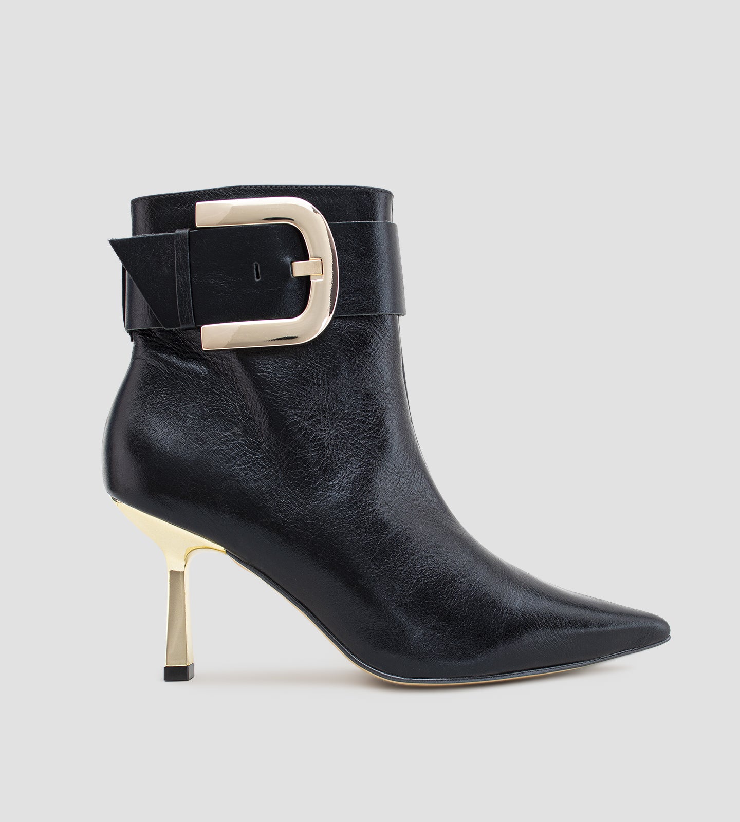 Bota feminina preta em couro, com bico fino, salto alto fino e detalhe de fivela larga dourada no tornozelo.