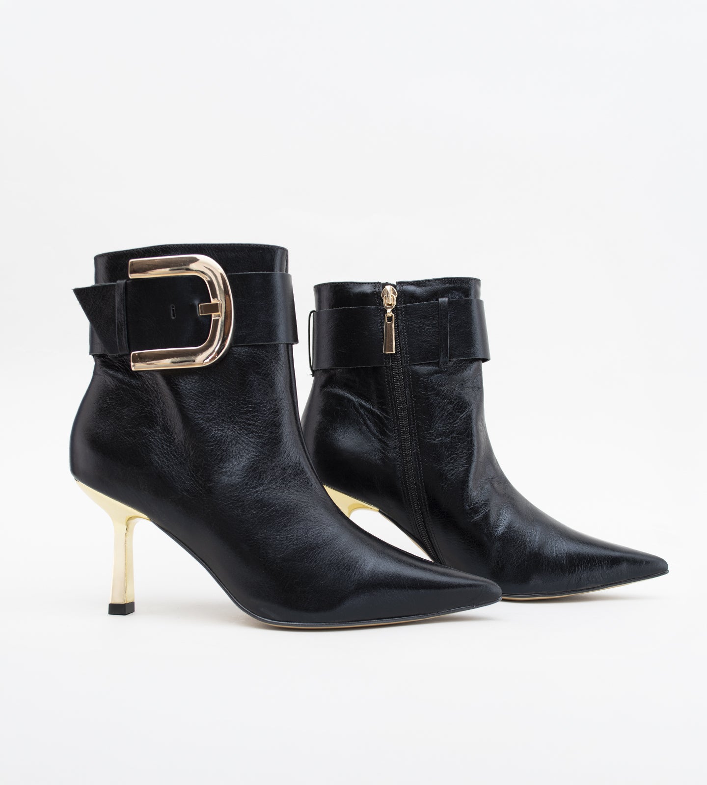 Bota feminina preta em couro, com bico fino, salto alto fino e detalhe de fivela larga dourada no tornozelo.