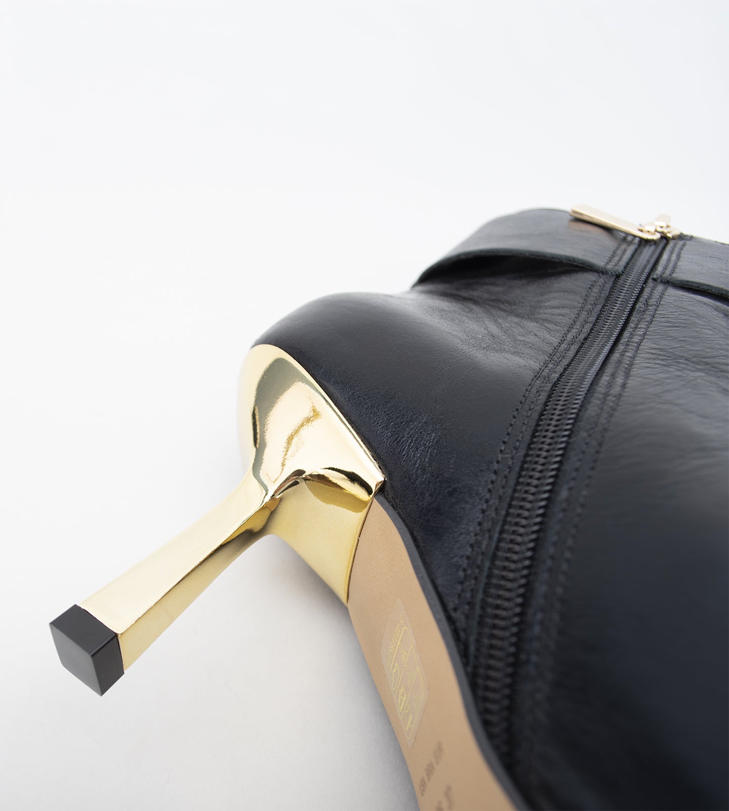 Bota feminina preta em couro, com bico fino, salto alto fino e detalhe de fivela larga dourada no tornozelo.