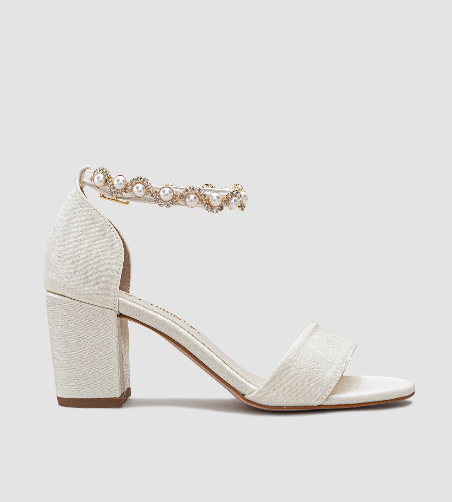 Sandália de noiva off-white em tecido velvet com brilho sutil, salto grosso de 7 cm, tira larga nos dedos e tornozeleira com pérolas e brilhos, unindo conforto, elegância e sofisticação para o grande dia.