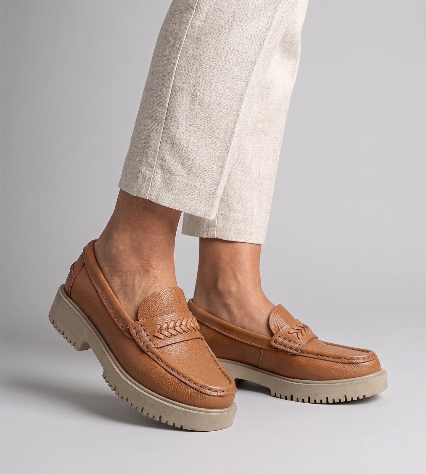 Mocassim feminino em couro marrom com solado tratorado e detalhe trançado em couro, usado com calça clara em look moderno.
