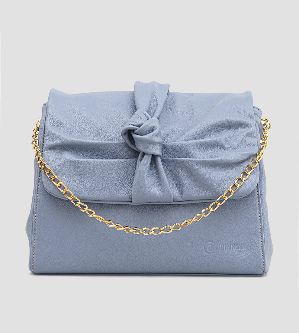 Bolsa feminina em couro azul com detalhe de nó, corrente dourada e alça ajustável, usada no ombro.