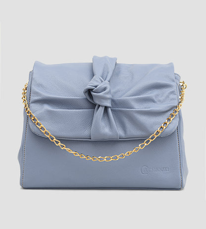 Bolsa feminina em couro azul com detalhe de nó, corrente dourada e alça ajustável, usada no ombro.