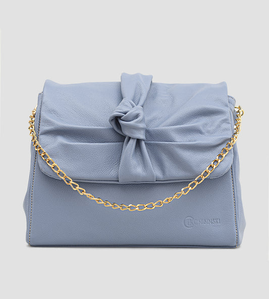 Bolsa feminina em couro azul com detalhe de nó, corrente dourada e alça ajustável, usada no ombro.