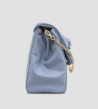 Bolsa feminina em couro azul com detalhe de nó, corrente dourada e alça ajustável, usada no ombro.