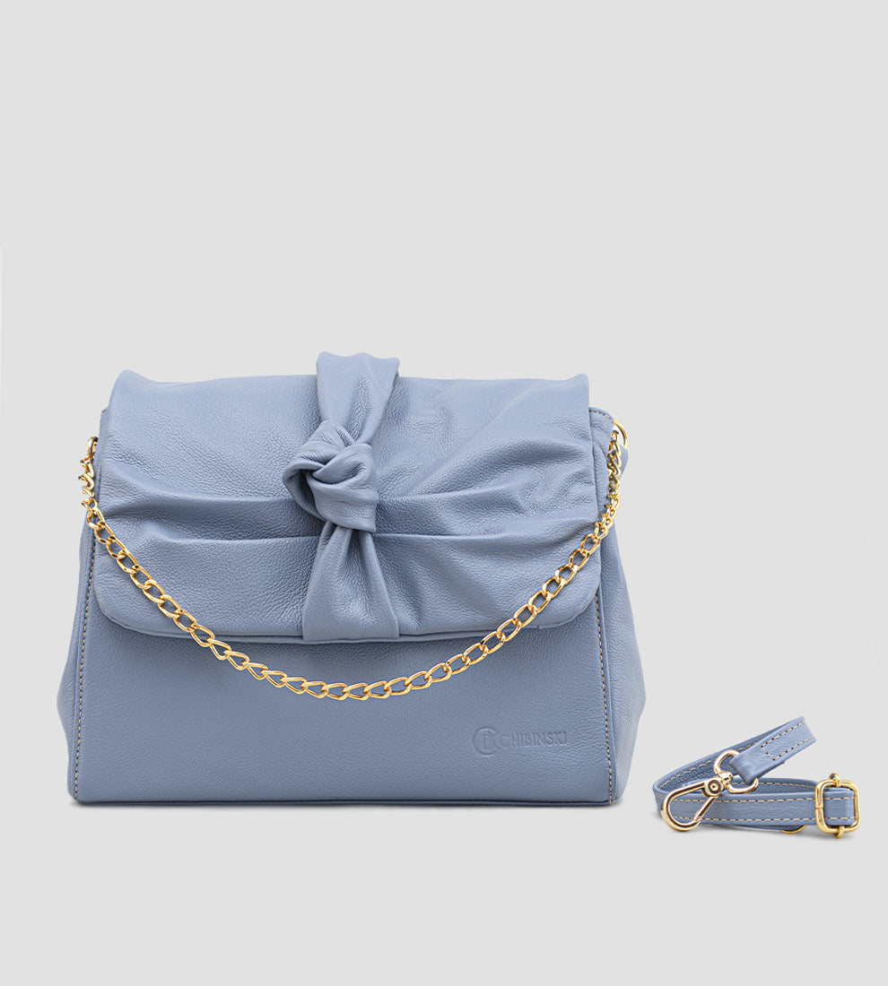 Bolsa feminina em couro azul com detalhe de nó, corrente dourada e alça ajustável, usada no ombro.