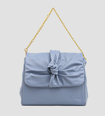 Bolsa feminina em couro azul com detalhe de nó, corrente dourada e alça ajustável, usada no ombro.