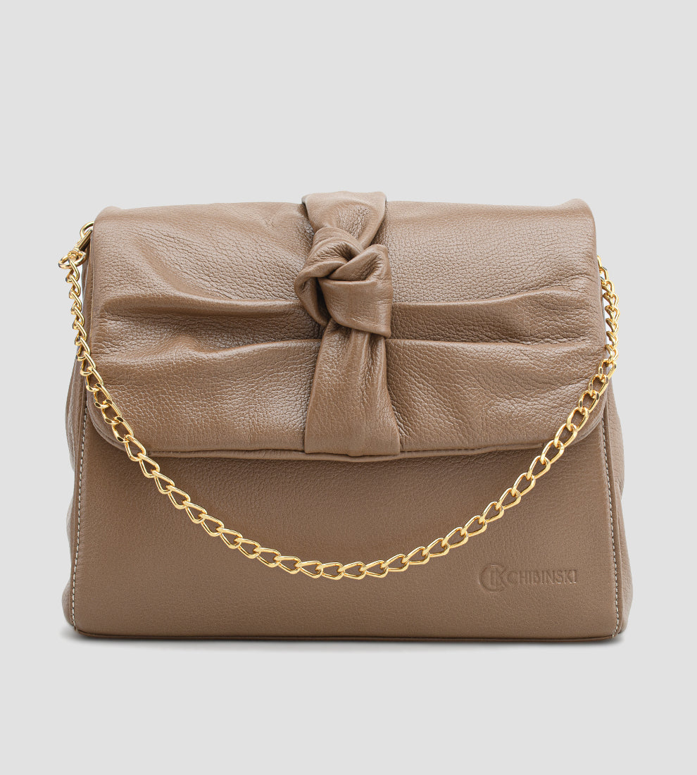 Bolsa feminina em couro marrom com detalhe de nó, corrente dourada e alça ajustável, usada no ombro.