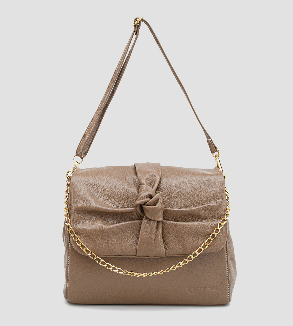 Bolsa feminina em couro marrom com detalhe de nó, corrente dourada e alça ajustável, usada no ombro.