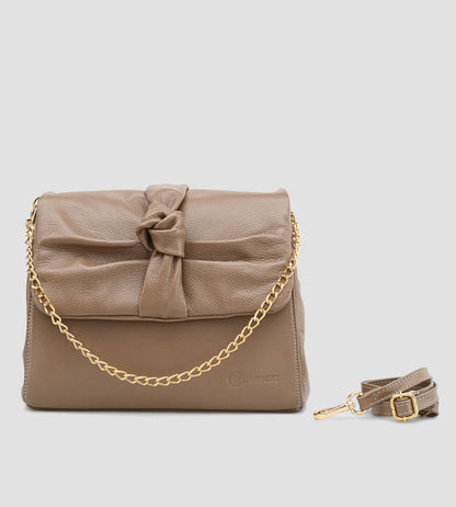Bolsa feminina em couro marrom com detalhe de nó, corrente dourada e alça ajustável, usada no ombro.