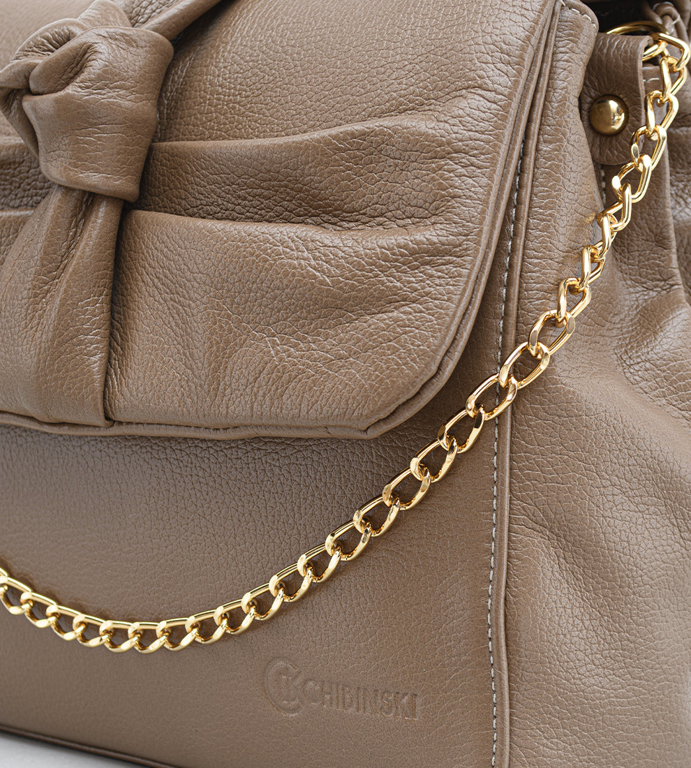 Bolsa feminina em couro marrom com detalhe de nó, corrente dourada e alça ajustável, usada no ombro.