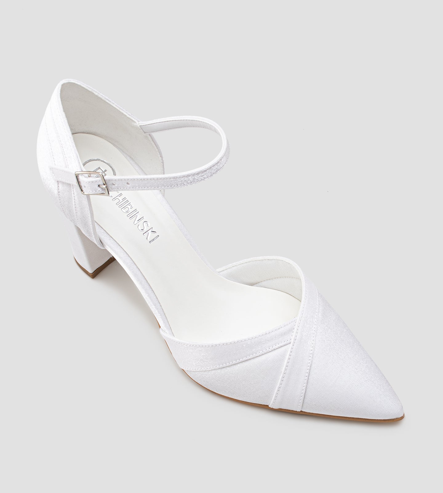 Sapato de noiva scarpin branco em tecido velvet, com bico fino, salto bloco médio de 7 cm e tira no tornozelo com fivela, exibido nos pés com calça clara.