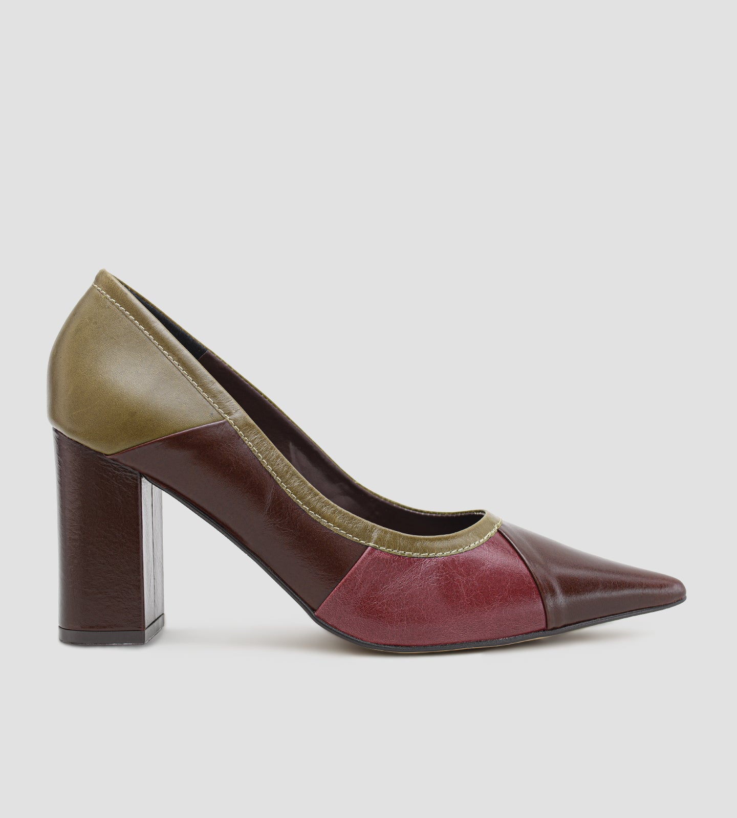 Vista lateral de um scarpin feminino de couro. O modelo apresenta bico fino, salto bloco grosso na cor marrom e uma composição em color block com recortes de couro em marrom escuro, vinho e verde-oliva na parte traseira e nas bordas do calce. Fundo liso em tom cinza claro.