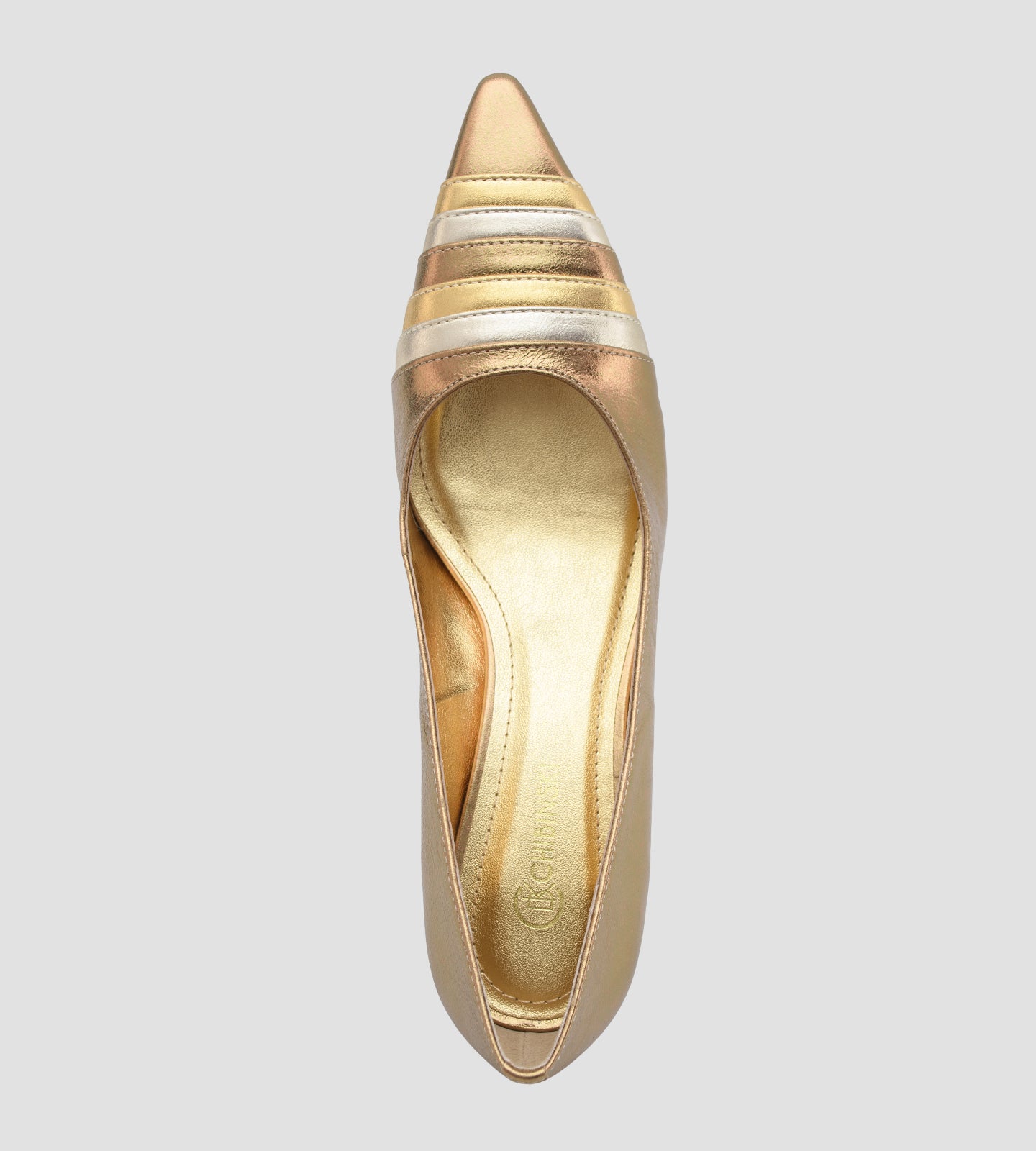scarpin feminino de couro na cor bronze metalizado. O sapato possui bico fino com um detalhe frontal de tiras metálicas sobrepostas em tons alternados de dourado claro e bronze. O salto é médio, de 7cm, com um design fino que se alarga levemente na base. Fundo liso cinza claro.