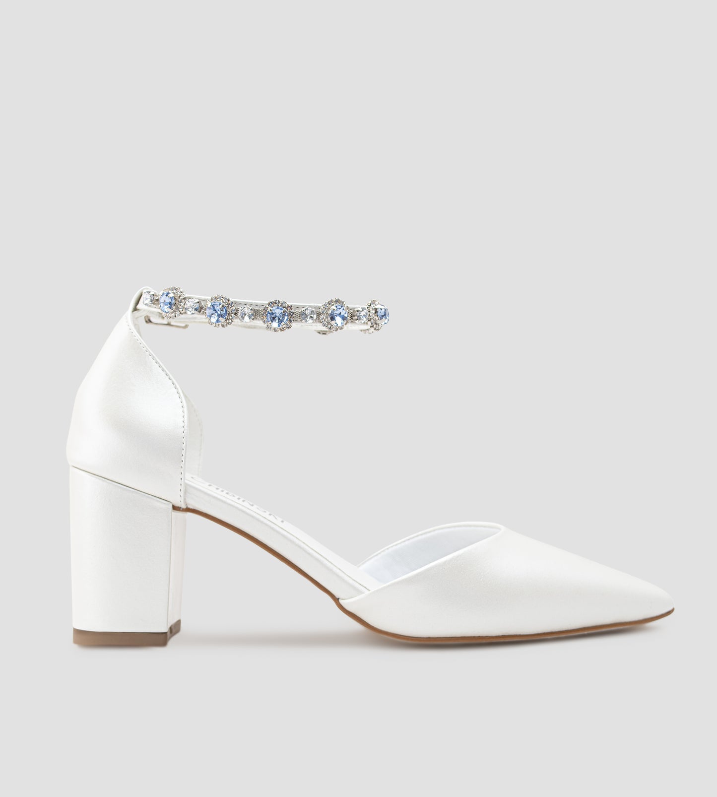 Sapato de noiva em couro branco perolado com bico fino, salto bloco médio e pulseira no tornozelo adornada com cristais azul-claro, ideal para casamento, fotografado em fundo cinza claro.