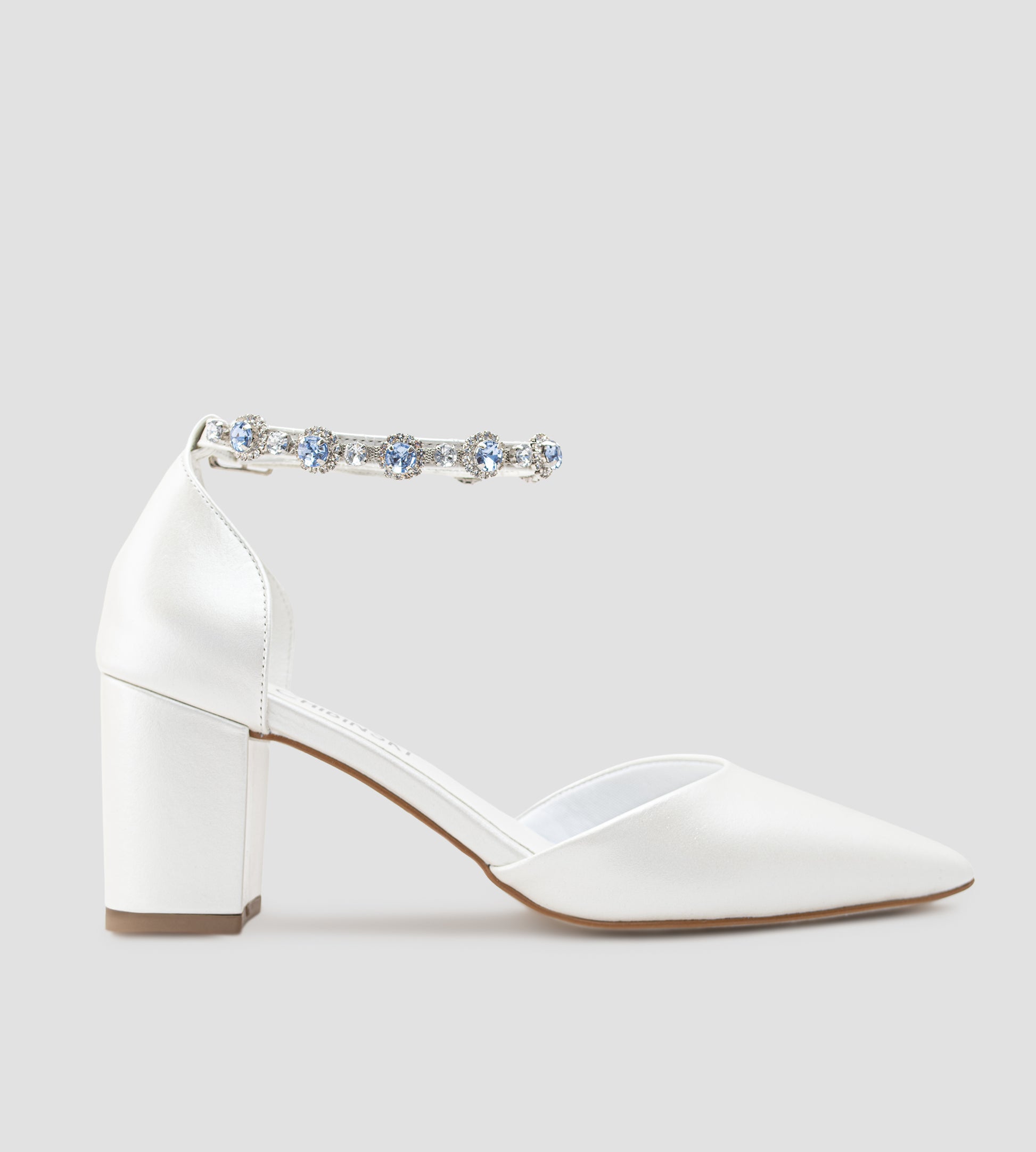 Sapato de noiva em couro branco perolado com bico fino, salto bloco médio e pulseira no tornozelo adornada com cristais azul-claro, ideal para casamento, fotografado em fundo cinza claro.