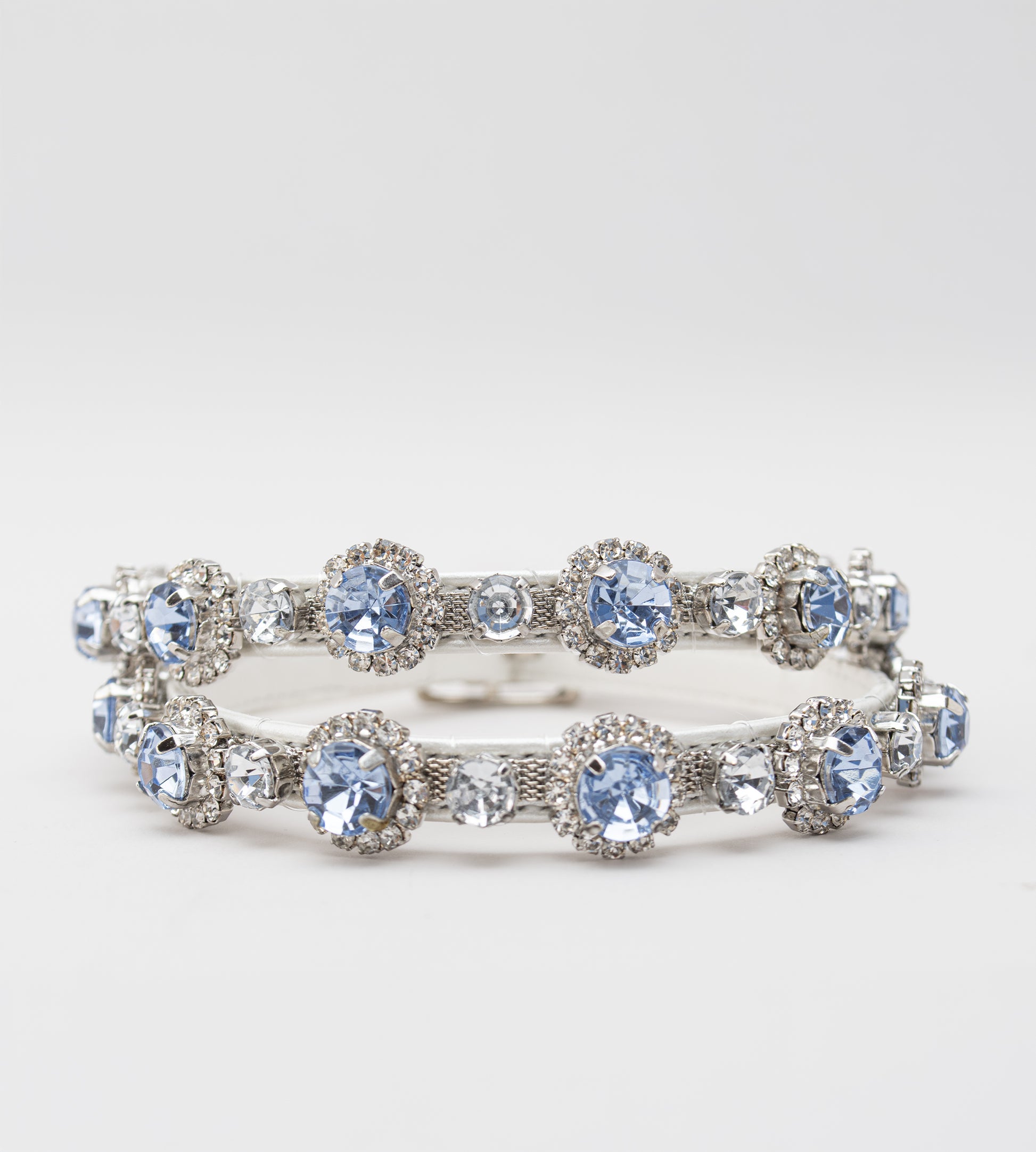 Sapato de noiva em couro branco perolado com bico fino, salto bloco médio e pulseira no tornozelo adornada com cristais azul-claro, ideal para casamento, fotografado em fundo cinza claro.