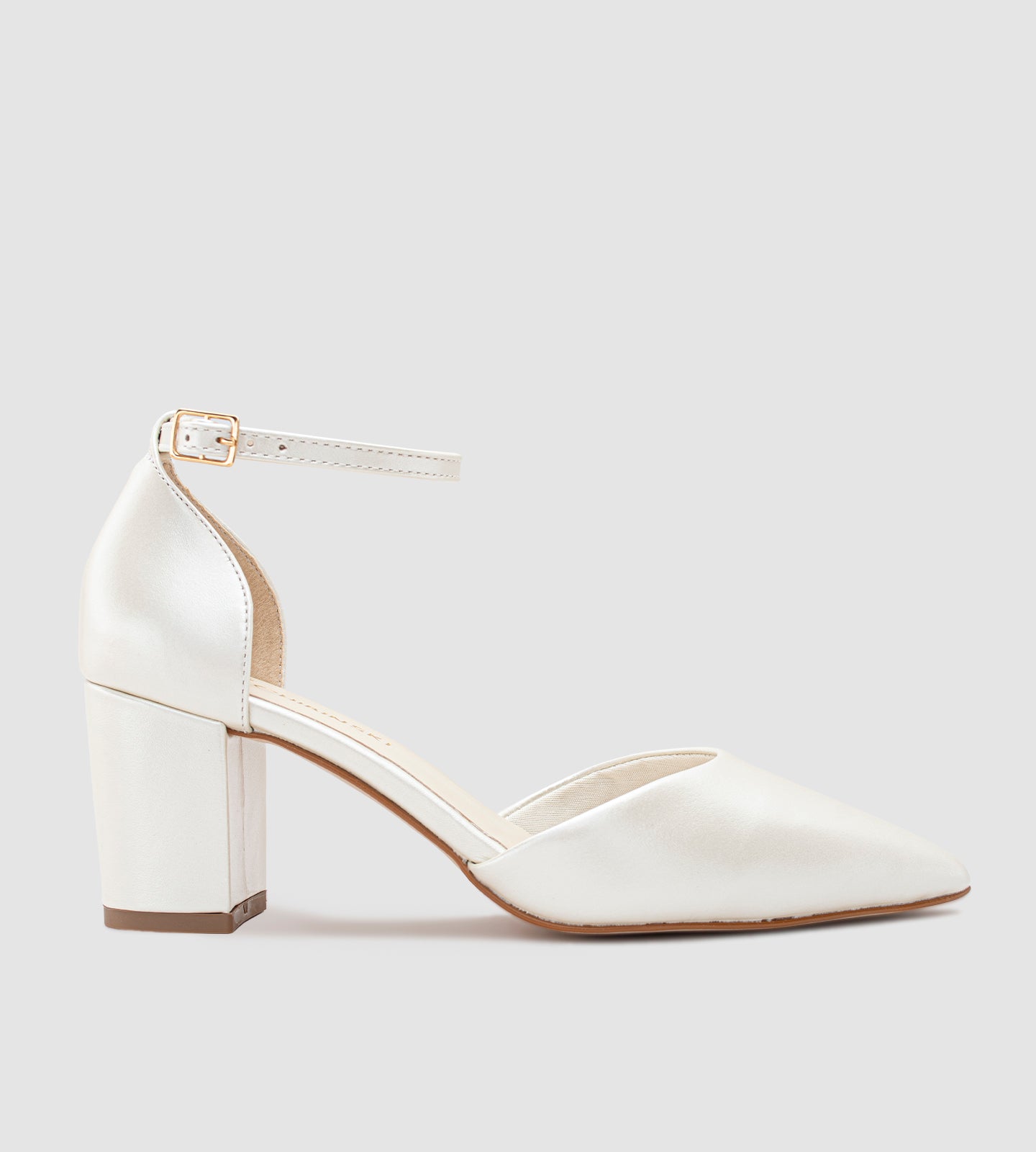 Imagem de um scarpin de noiva na cor off-white com acabamento em couro perolado. O sapato possui bico fino, salto bloco médio e uma tira com fivela dourada ajustável no tornozelo. O design é elegante e minimalista, ideal para casamentos e eventos especiais.