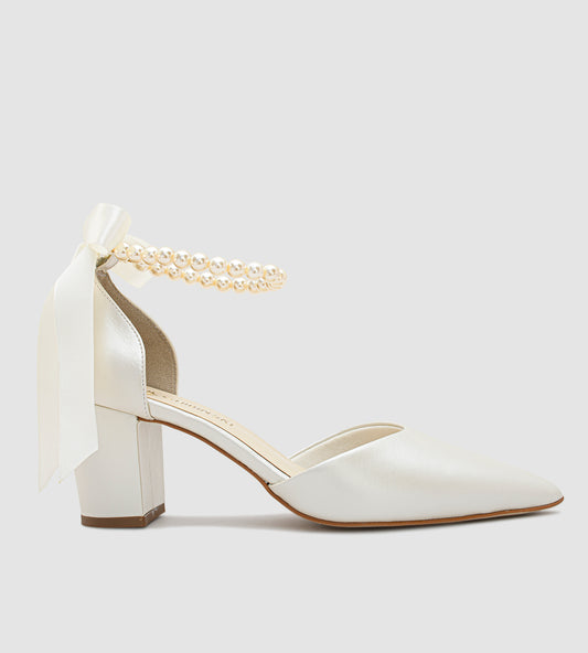 Sandália de noiva em couro perolado off white com salto bloco de 7cm, bico fino e tornozeleira de pérolas com laço de cetim, ideal para casamento.
