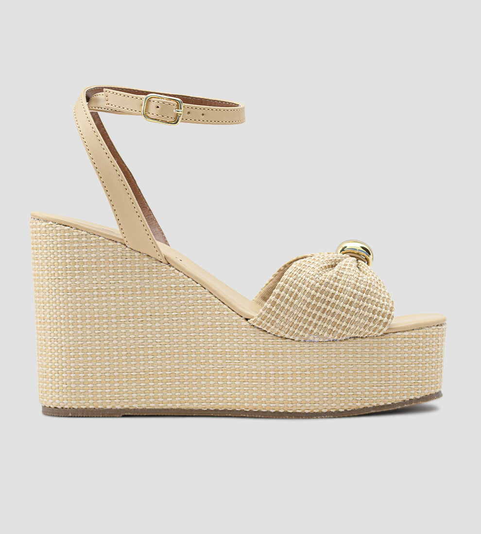Sandália anabela nude feminina com salto plataforma revestido em palha, tira frontal com nó e fecho de fivela no tornozelo, estilo elegante e confortável para o verão.