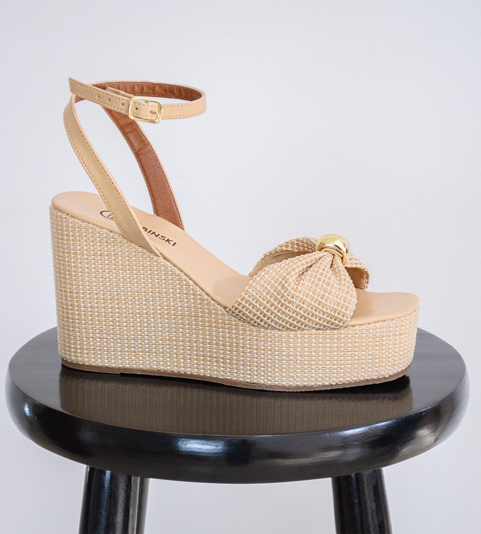 Sandália anabela nude feminina com salto plataforma revestido em palha, tira frontal com nó e fecho de fivela no tornozelo, estilo elegante e confortável para o verão.