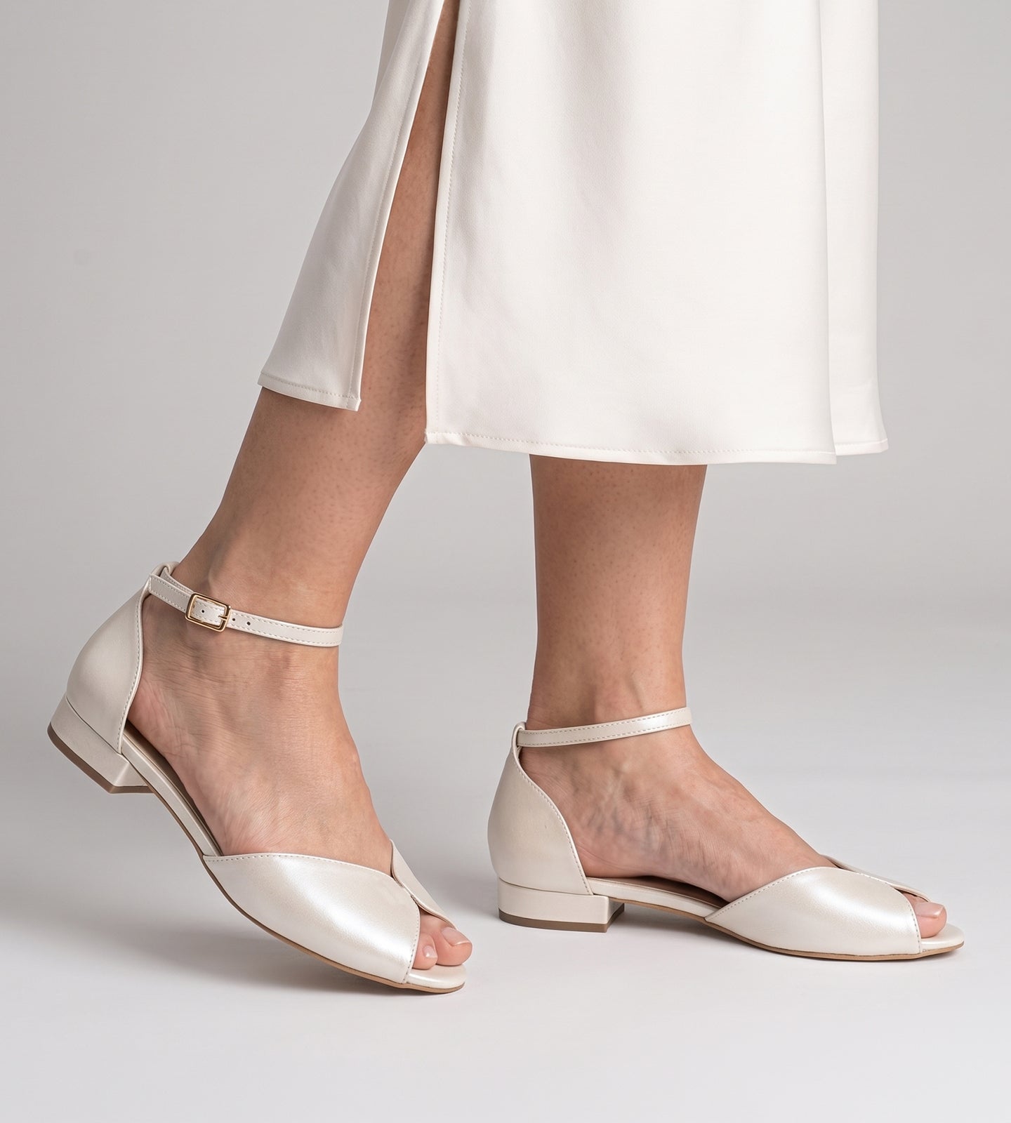 Sandália de noiva estilo sapatilha em couro perolado off white, com bico aberto, tira no tornozelo com fivela e solado baixo, sem salto.