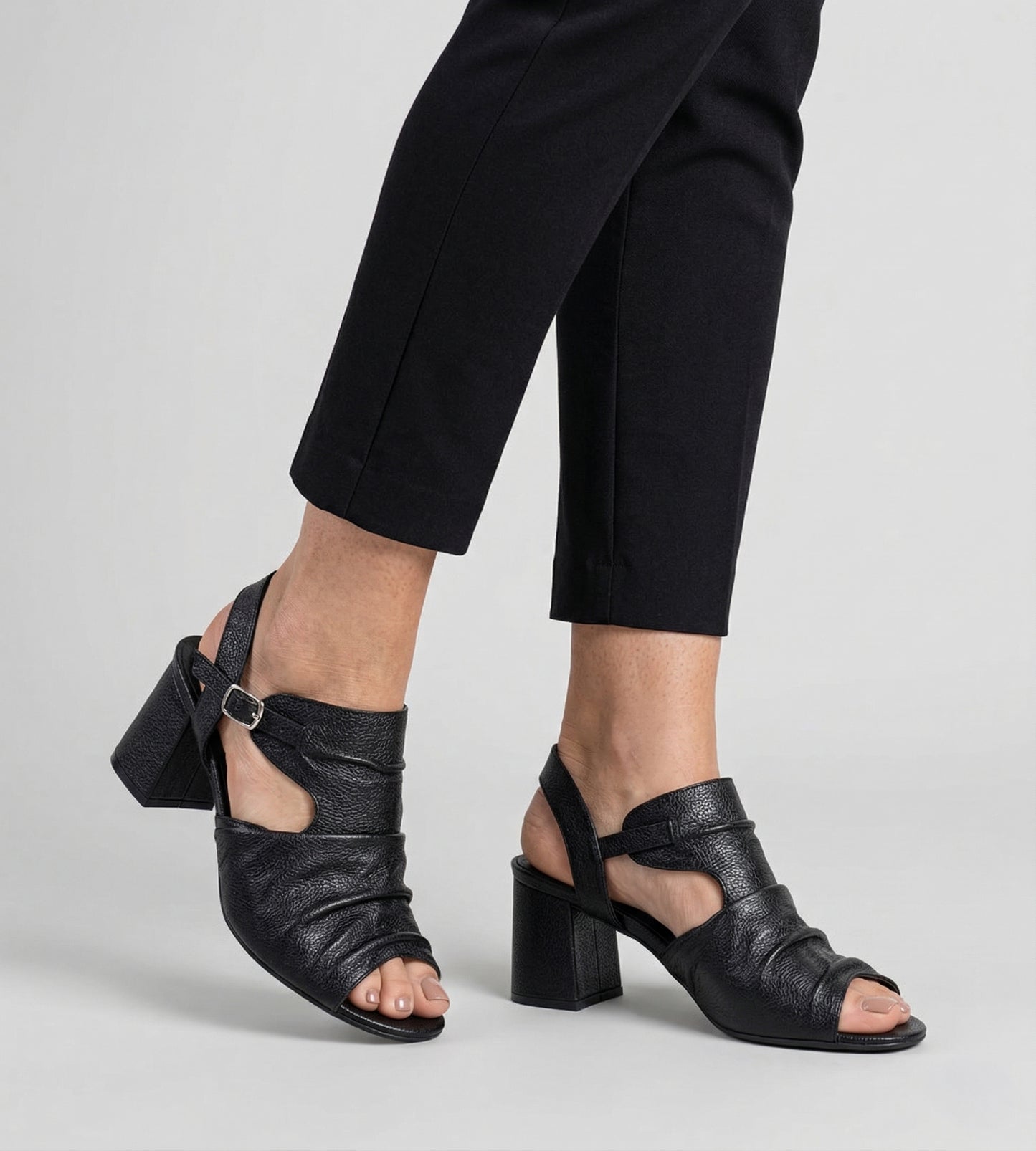 sandália ankle boot feminina preta em couro com salto bloco médio e tiras, vista lateral nos pés com calça preta, estilo elegante e confortável.