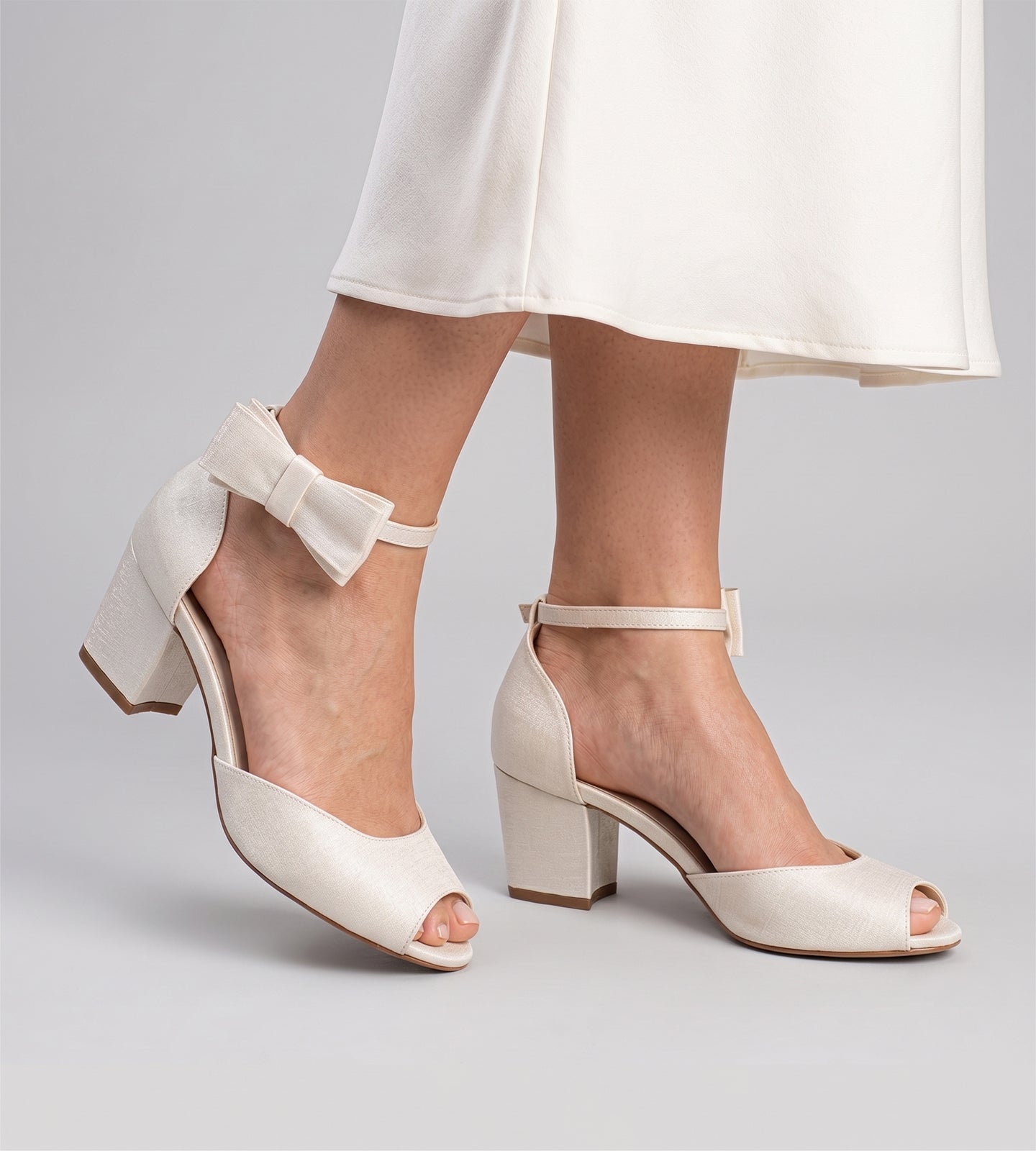 Sandália de noiva em tecido velvet off white, com bico aberto, salto baixo de 5 cm e tira no tornozelo com laço removível.