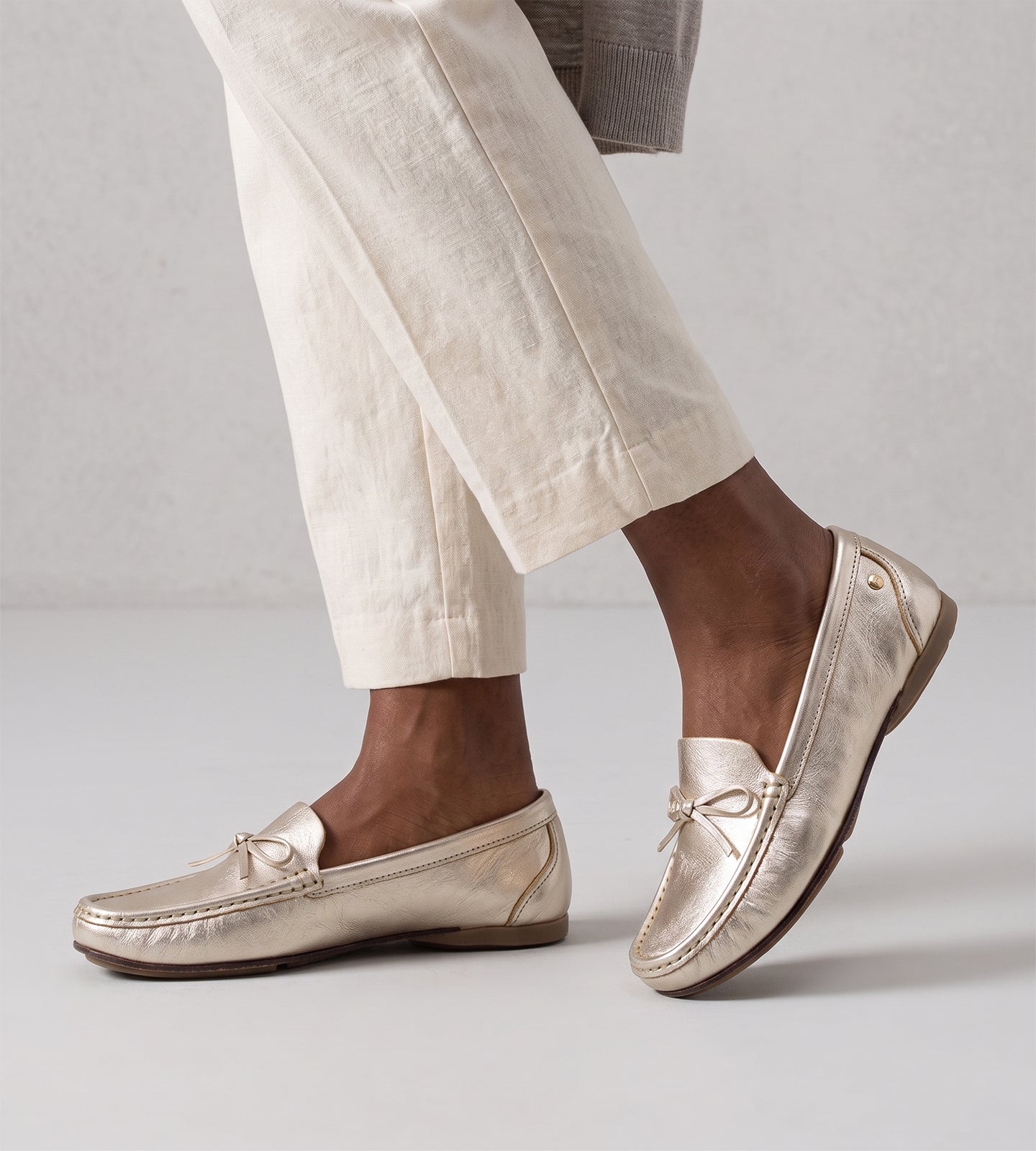 Mocassim feminino em couro legítimo dourado com laço frontal, acabamento sofisticado e design slip-on, ideal para looks elegantes e confortáveis no dia a dia.