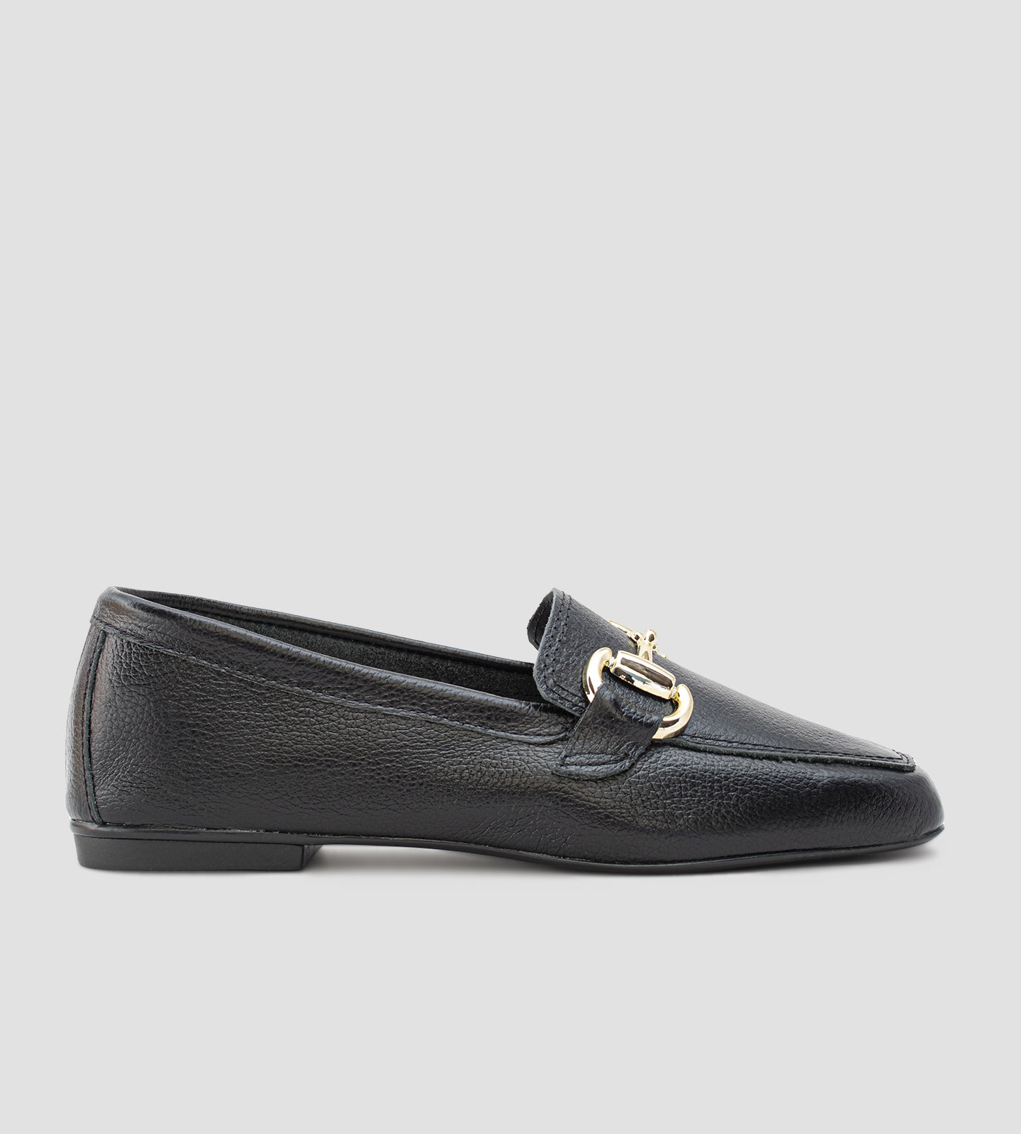 Mocassim feminino preto em couro legítimo com detalhe metálico dourado frontal e solado baixo, usado com calça clara em composição elegante e sofisticada.