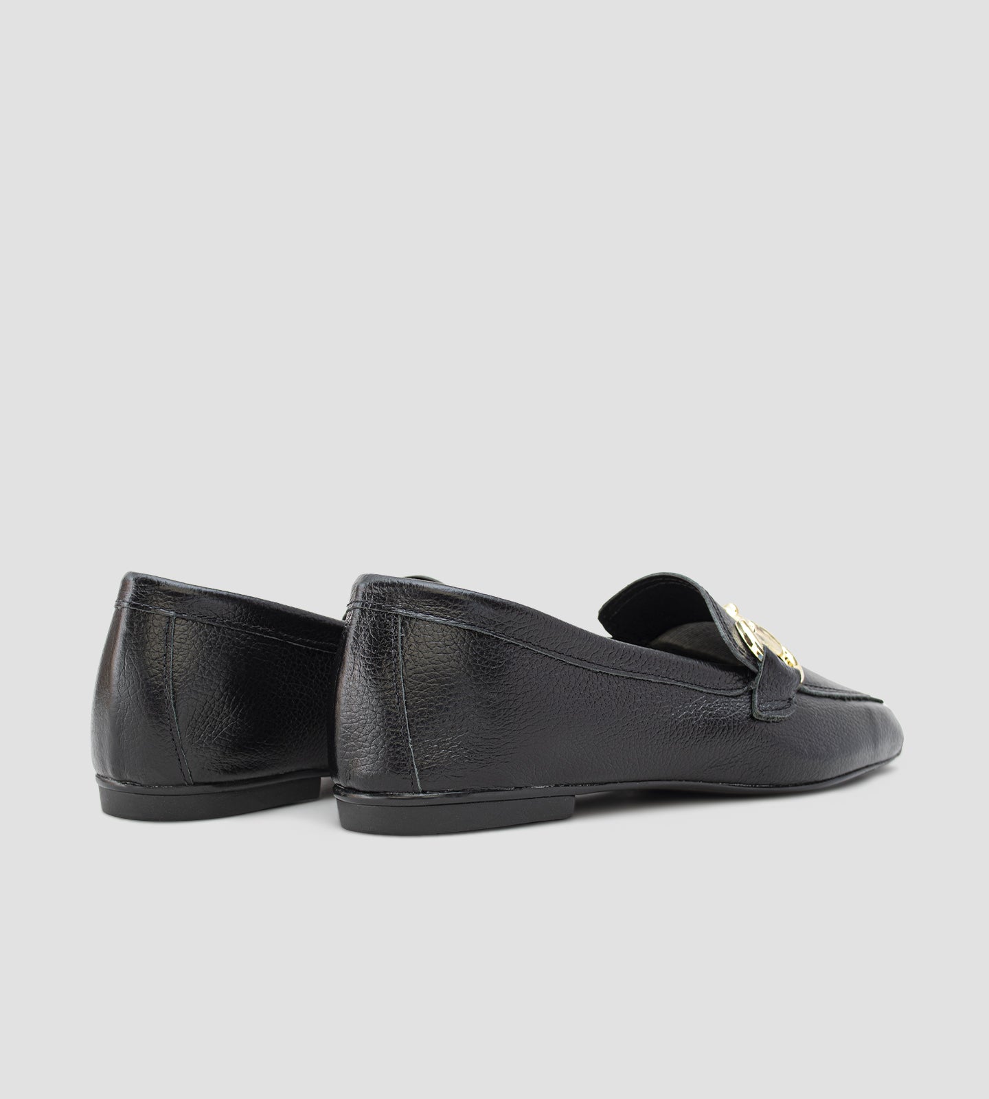 Mocassim feminino preto em couro legítimo com detalhe metálico dourado frontal e solado baixo, usado com calça clara em composição elegante e sofisticada.